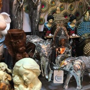 A collection of decorative figurines, prominently showcasing the elegant Silver Elephant from Thailand, accompanied by graceful angels and refined busts, all tastefully arranged on a shelf.