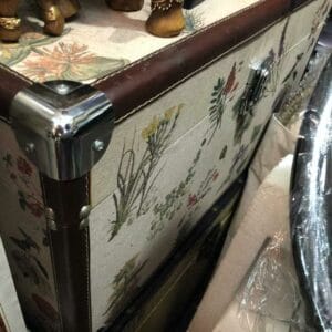 A partially visible Floral Chest - Pink, adorned with elegant floral patterns and metal corners, is nestled among various home decor items, adding a touch of Dapitan charm.