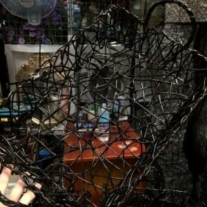 A hand reaches for a Black Container - Small nestled among an eclectic mix of decor on a cluttered Dapitan shelf, with a fan softly whirring in the background.