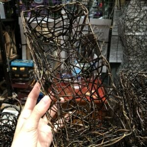 A hand gracefully holds a Black Container - Small, a charming piece of home decor, in a Dapitan store filled with various intriguing items in the background.