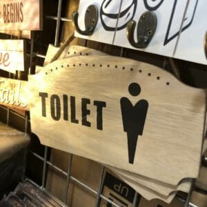Wooden sign featuring a male figure icon and the word "TOILET" in bold letters, positioned above a Black Container - Small, and adorned with decorative stars.