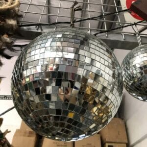 A black container in a small size sits on a mirrored disco ball hanging from a metal grid shelf in a storage area, offering an unexpected touch of decor. Boxes can be seen in the background, suggesting its journey to provide someone's home with an elegant touch of Dapitan charm.