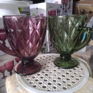 Two Colored Drinking Glasses, one in a textured purple and another in green, are elegantly placed on a decorative round table, adding a touch of chic home decor to your space.