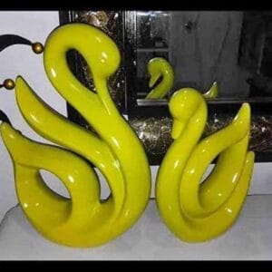 Two abstract Ceramic Swan Figurines in yellow are beautifully displayed on a reflective surface, accompanied by a mirror in the background. This elegant decor piece enhances your home with a touch of sophistication, reminiscent of Dapitan's artistic flair.