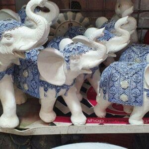 The Elephant Set Figurine, featuring ornate white elephants with blue decorations, brings a touch of elegance to your home decor when displayed on a Dapitan-inspired shelf.