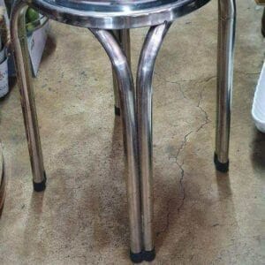 A 3 Foot Stainless Bar Stool with four legs stands elegantly on a cracked concrete floor, adding a touch of industrial charm to the home decor, reminiscent of unique finds from Dapitan.