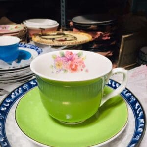 A Fancy Tea cup Set featuring a green teacup with a floral pattern on a matching saucer adds a touch of decor to the shelf, artfully stacked among various dishes.