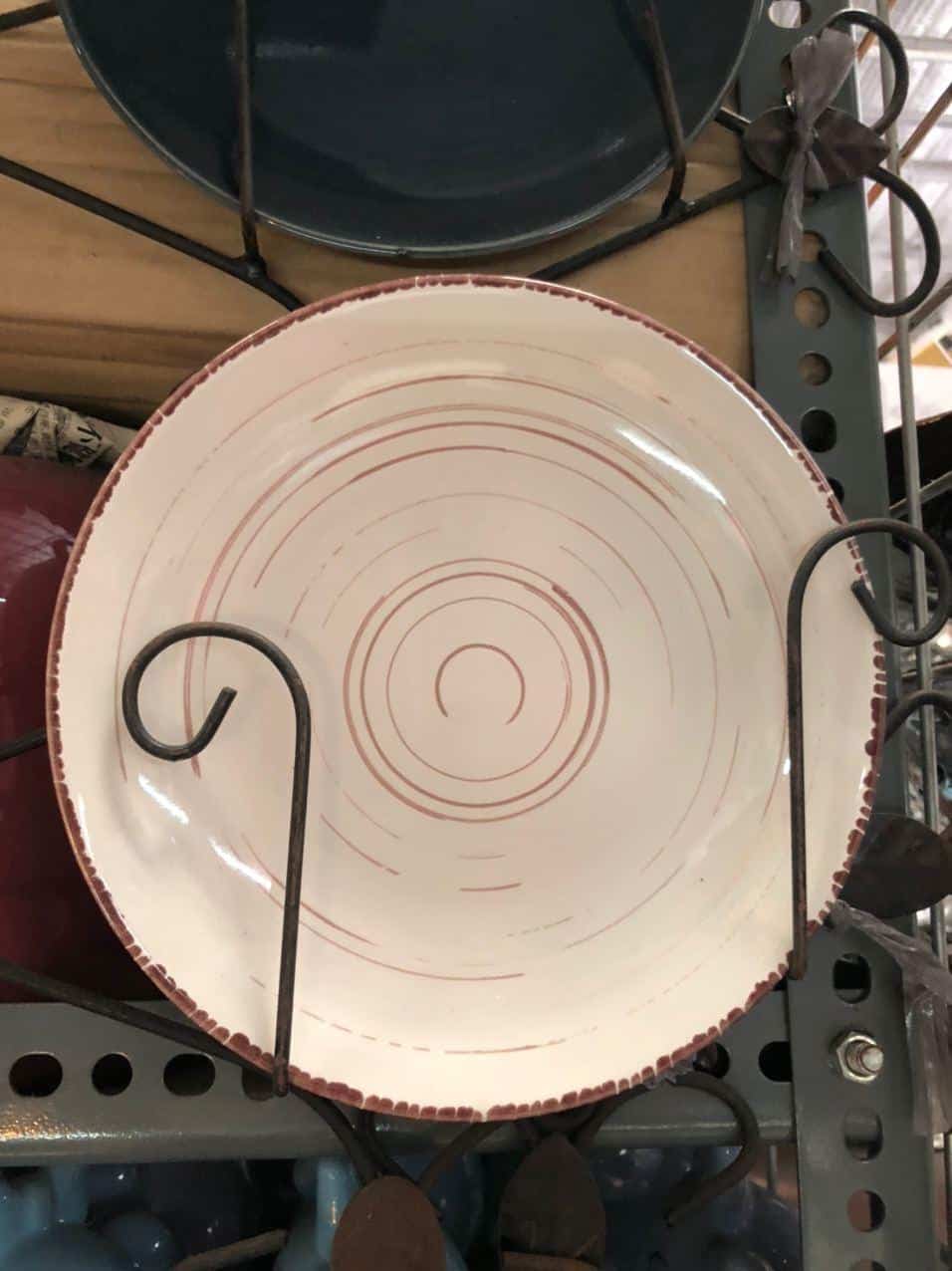 The Glossy Round Ceramic Plate, featuring a white base with a red spiral pattern, is displayed upright on a metal shelf, adding a touch of sophisticated decor to any home.