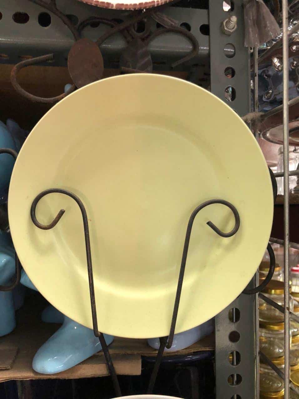 A Glossy Round Ceramic Plate in a dapitan-inspired yellow hue is elegantly displayed on a black metal stand, adding a touch of unique home decor to the store.