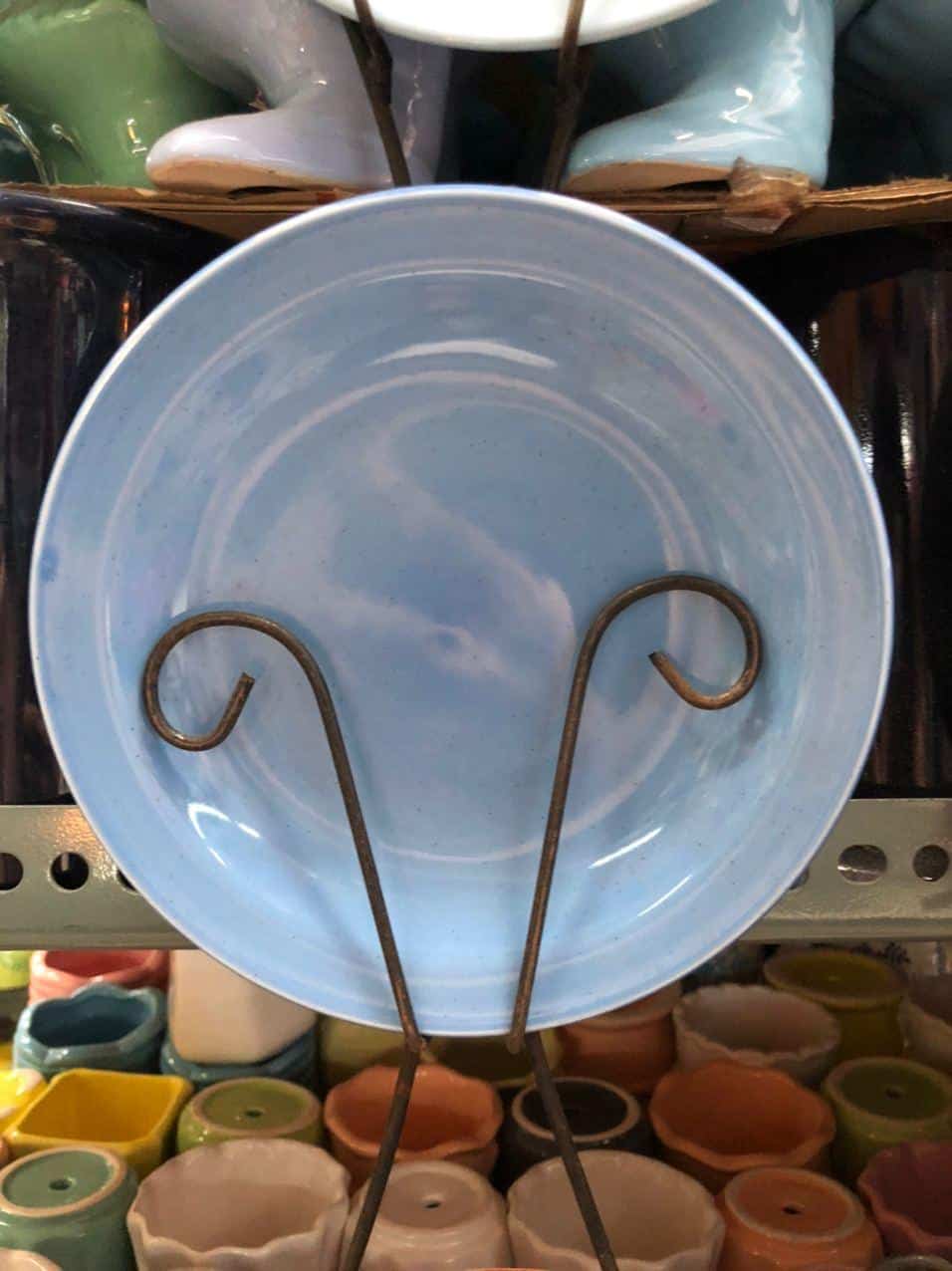 A Glossy Round Ceramic Plate in blue, a perfect piece of home decor, stands vertically on a shelf amid other colorful pottery treasures from Dapitan.