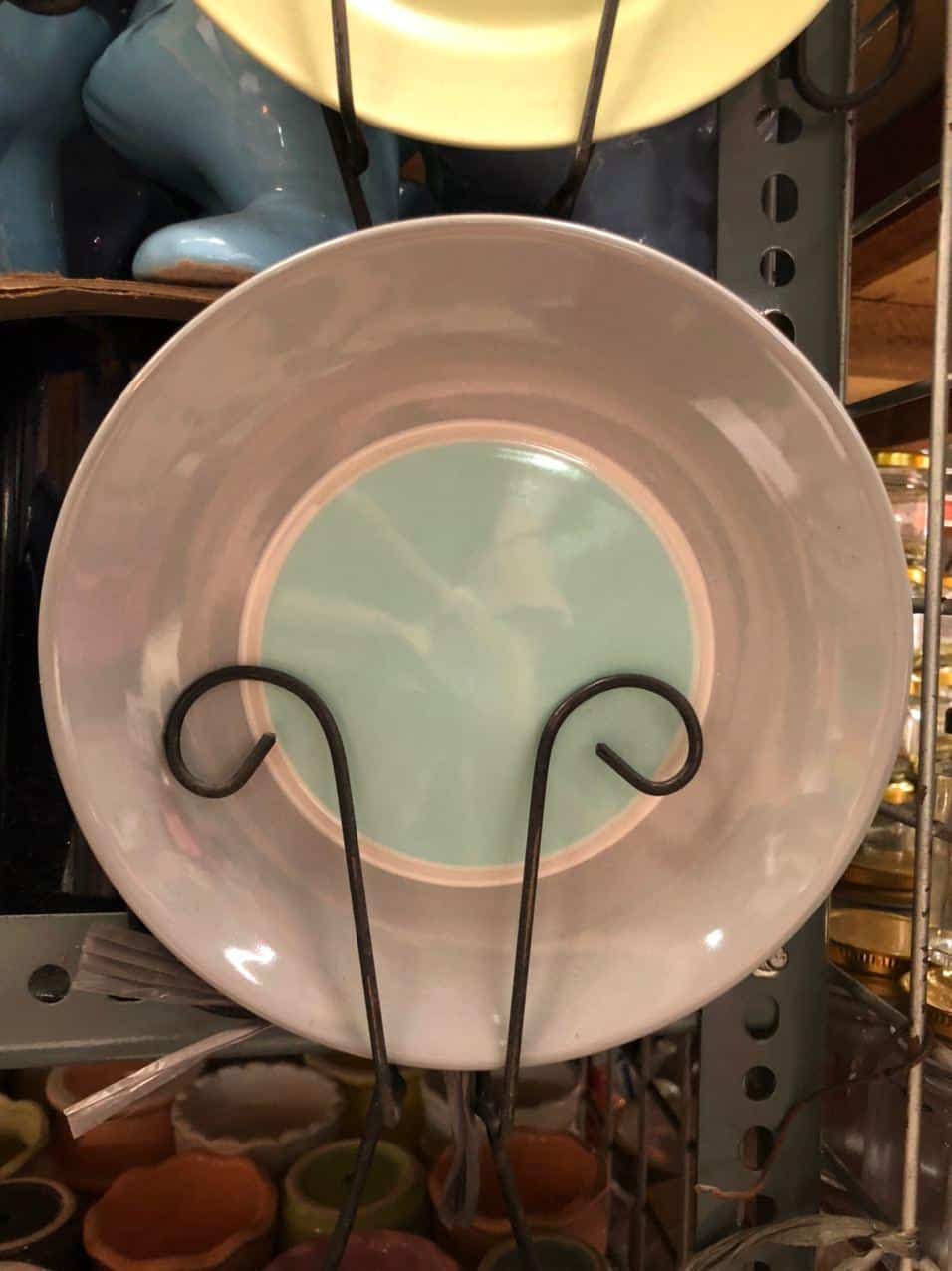 A Glossy Round Ceramic Plate, ideal for dapitan-inspired decor, is showcased on a metal stand within a store setting.