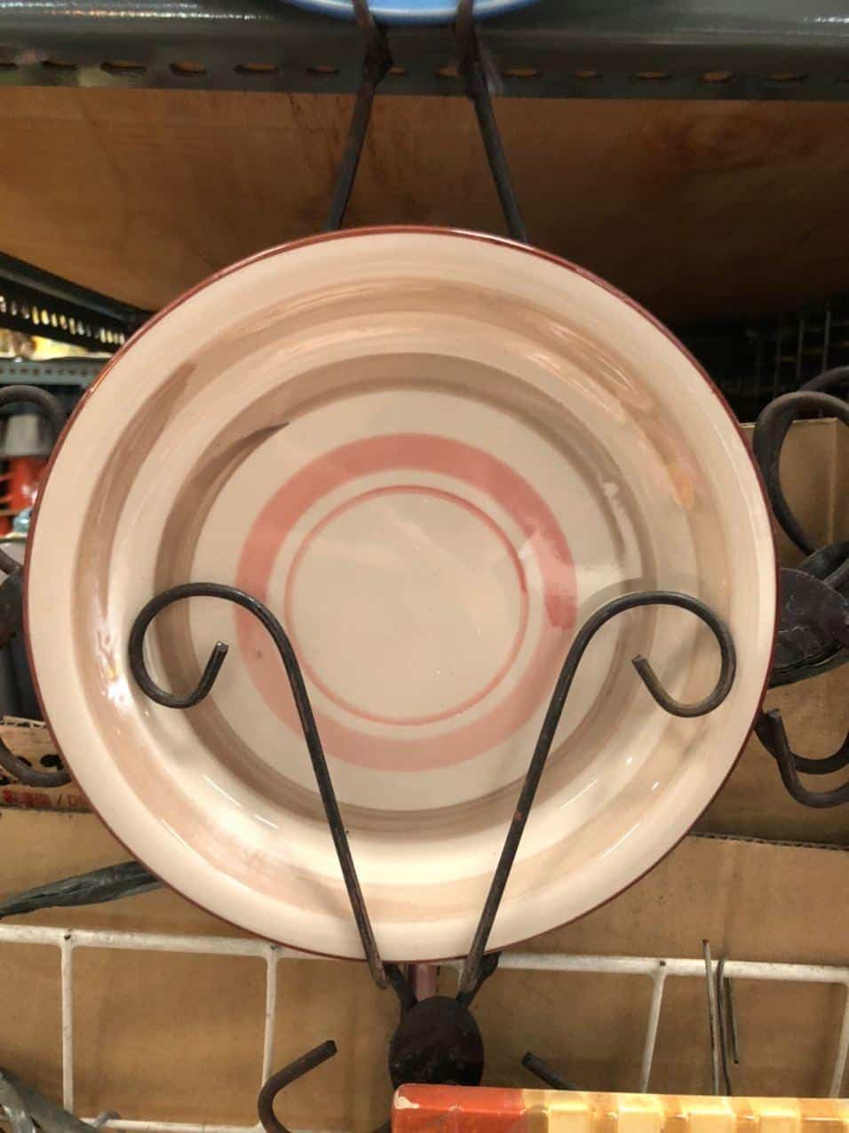The Glossy Round Ceramic Plate with pink concentric circles is displayed on a metal rack, adding a touch of delightful decor to your home.